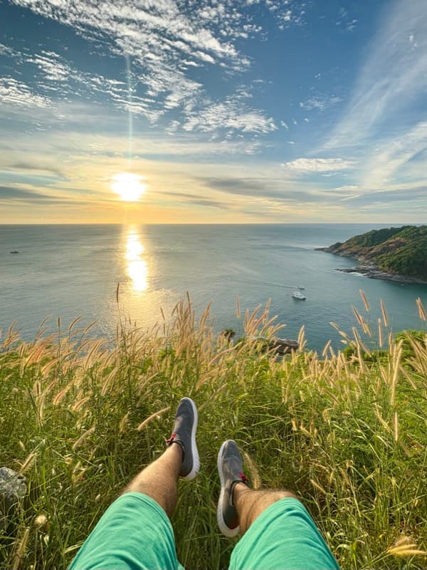 Feet up in tall grass above the sea at sunset
